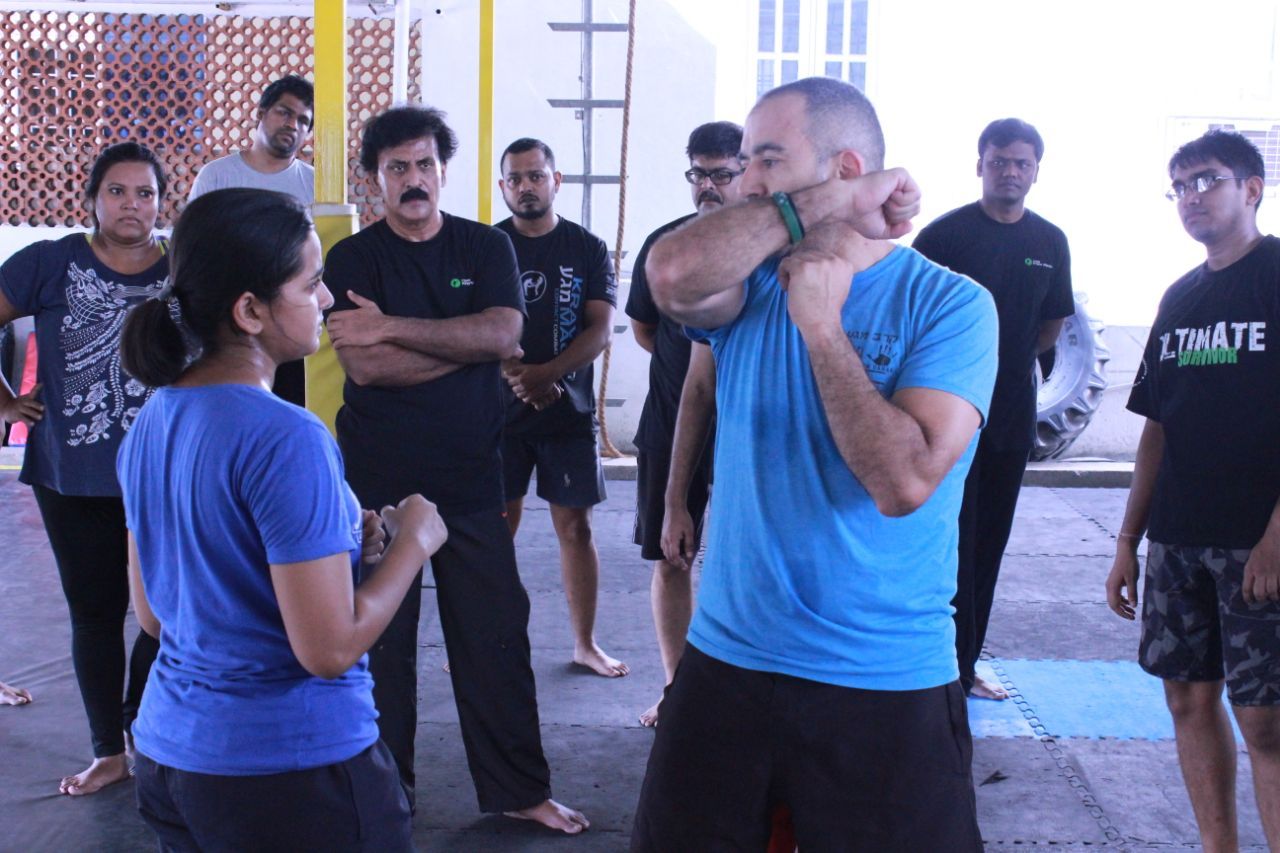 Krav Maga instructor demonstrating a guard position to a woman while participants watch