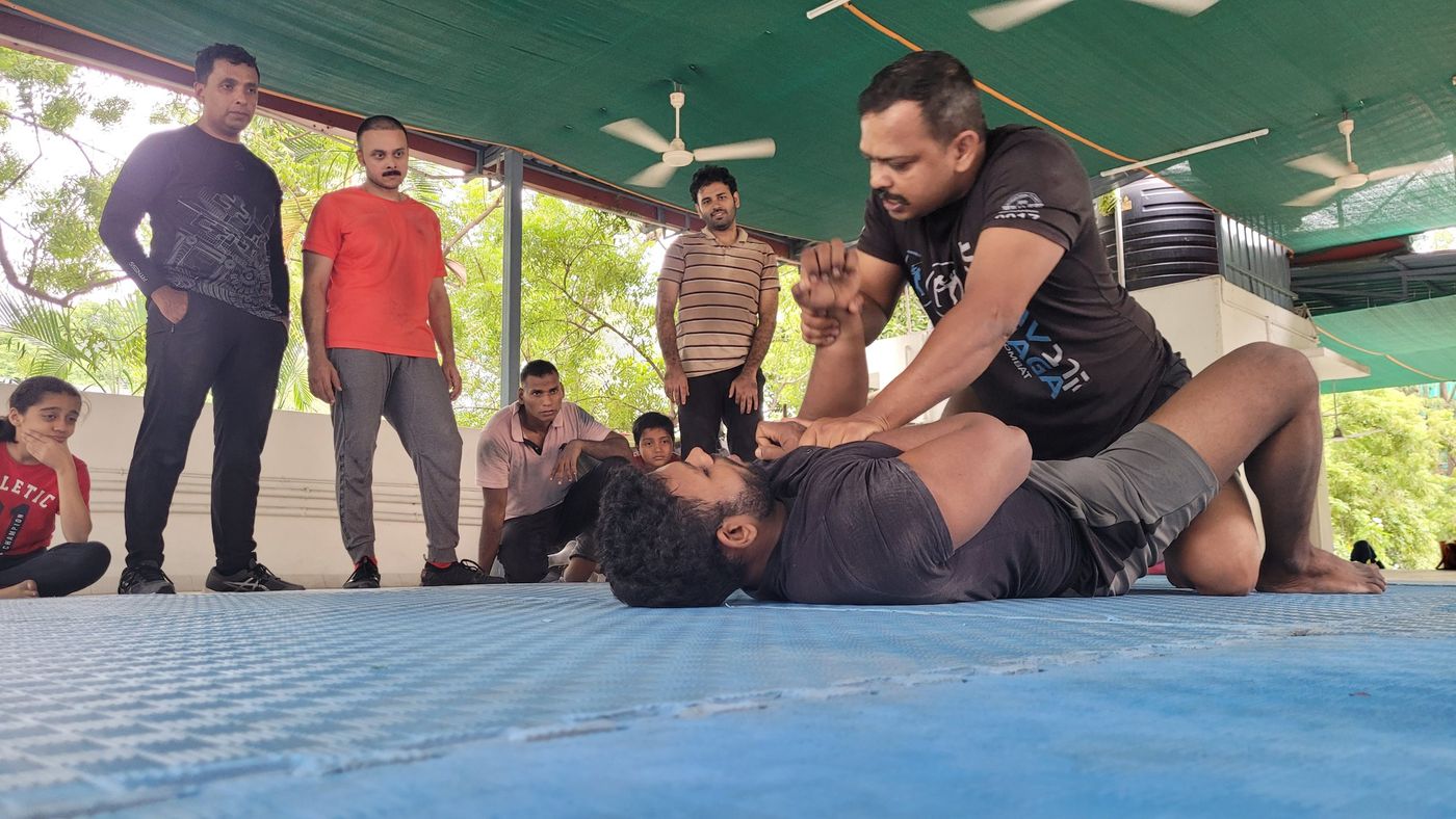 Krav Maga instructor demonstrating an arm control technique on the mat while participants watch